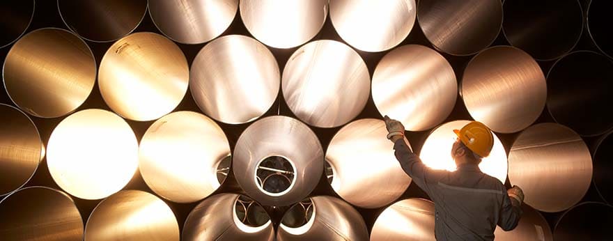 A factory worker is inspecting stacked steel pipes.