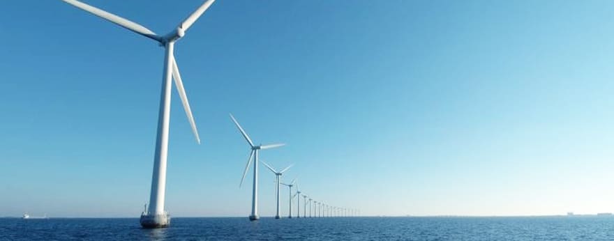 An image of wind power generators lined up over the sea.